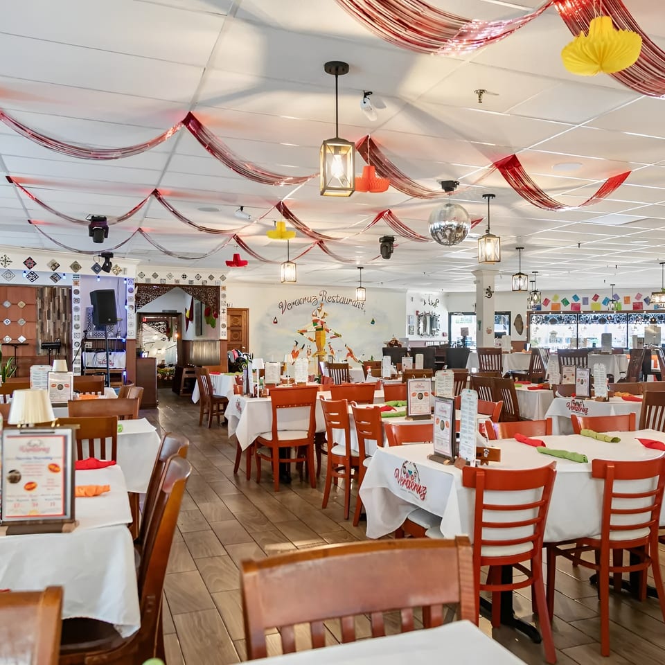 Spacious Veracruz Restaurant dining room with white tablecloths, orange chairs, and festive ceiling decorations.