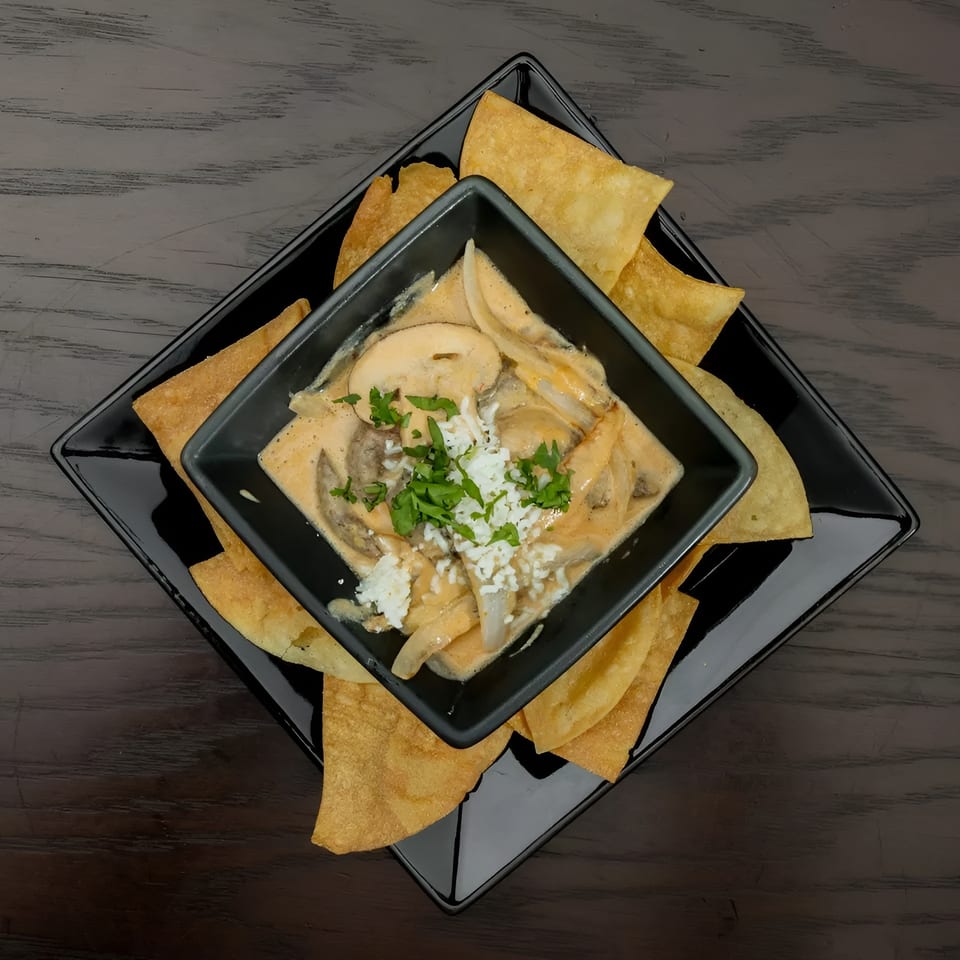 Mushroom and onion dip with crumbled cheese and parsley, served with tortilla chips on a black plate.