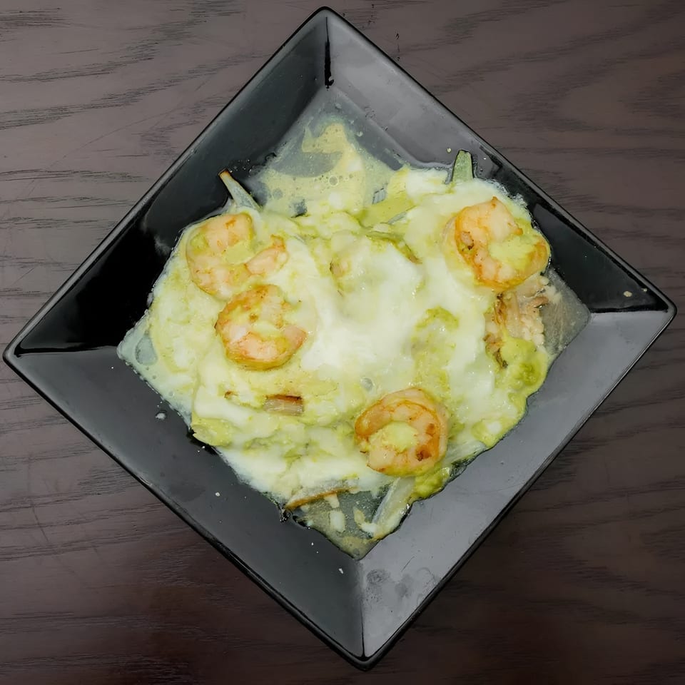 Shrimp dish with melted white cheese and green sauce on a black square plate.