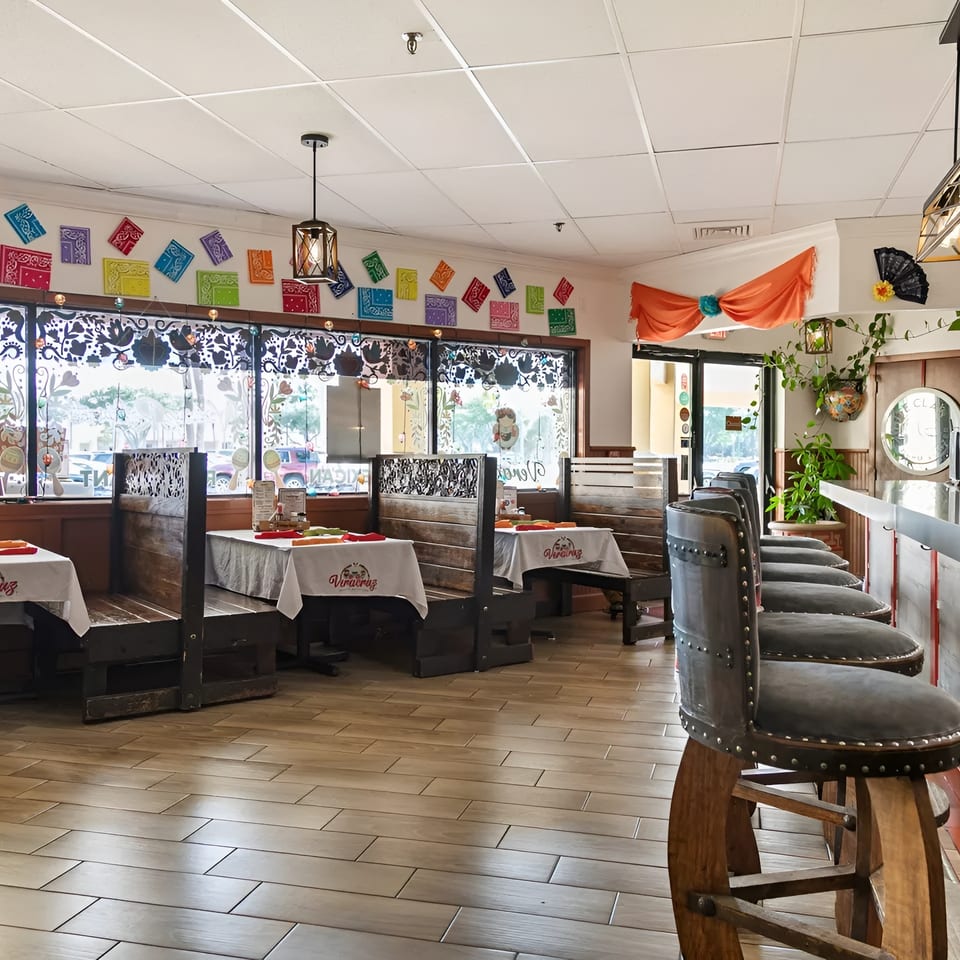Interior of a vibrant Mexican restaurant with colorful decor, wooden booths, and a bar with studded stools.