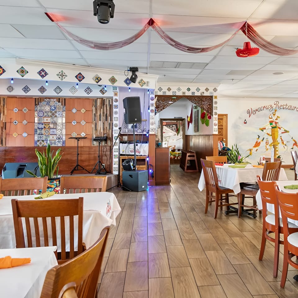 Interior of Veracruz Restaurant with dining tables, a stage, and a colorful mural on the wall.